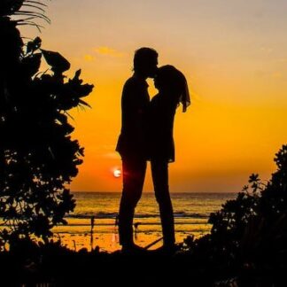 Photo of a silhouetted couple embracing on a beach at sunset.