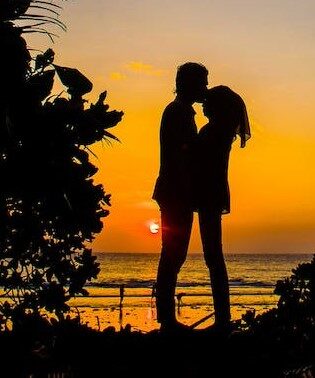 Photo of a silhouetted couple embracing on a beach at sunset.